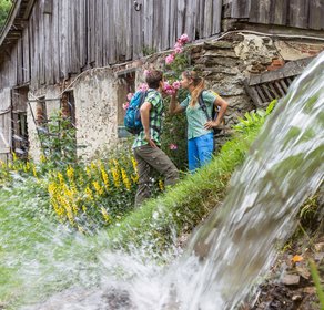 Ein Paar steht vor einem alten Gebäute und riecht an den rosa Rosen, die dort wachsen, im Vordergrund sieht man einen kleinen Wasserfall