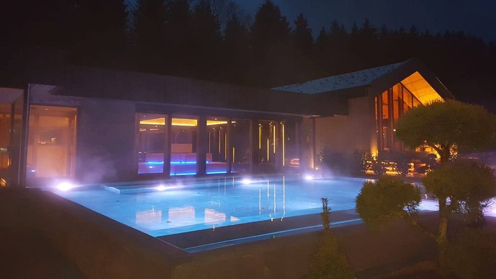 Blick auf das Saunahaus vom Bayerwaldhof bei Nacht, vor dem Saunahaus befindet sich ein dampfender Pool