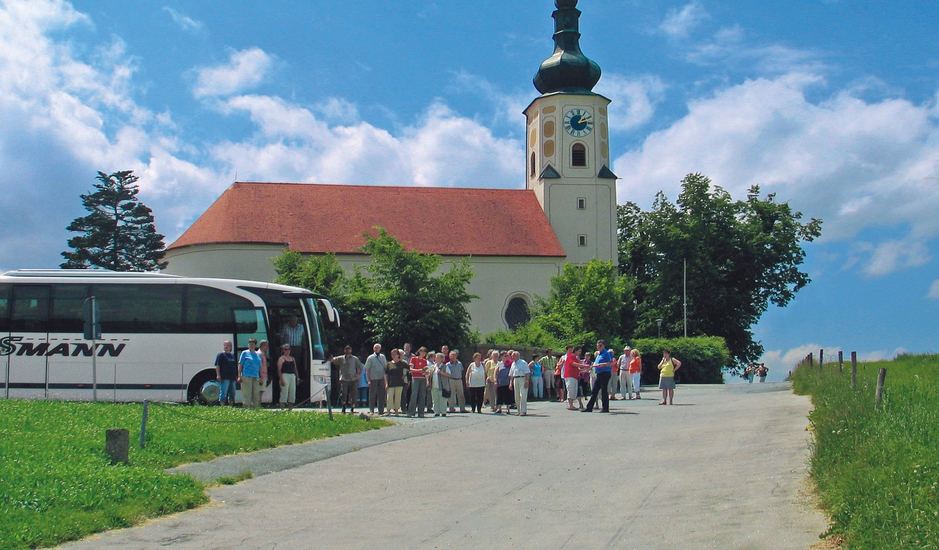 Gruppenreisen Blick auf die Wallfahrtskirche, davor steht eine Reisegruppe mit Bus