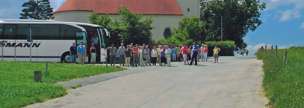 Blick auf die Wallfahrtskirche, davor steht eine Reisegruppe mit Bus