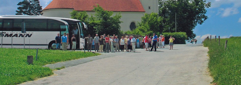 Blick auf die Wallfahrtskirche, davor steht eine Reisegruppe mit Bus