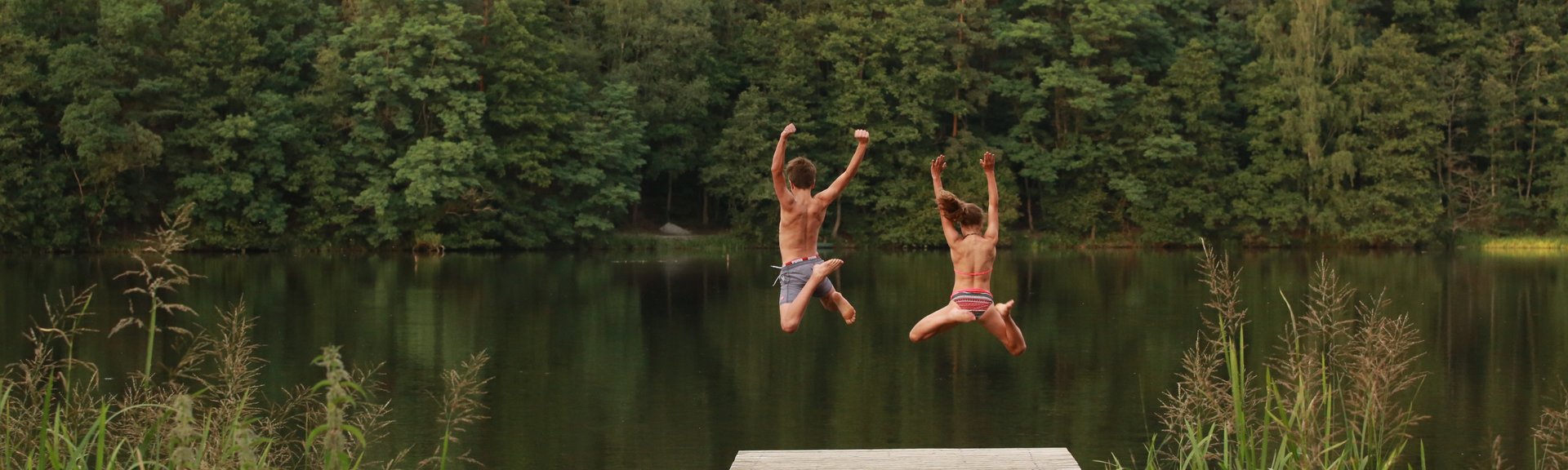 zwei Kinder springen vom Steg aus in den See