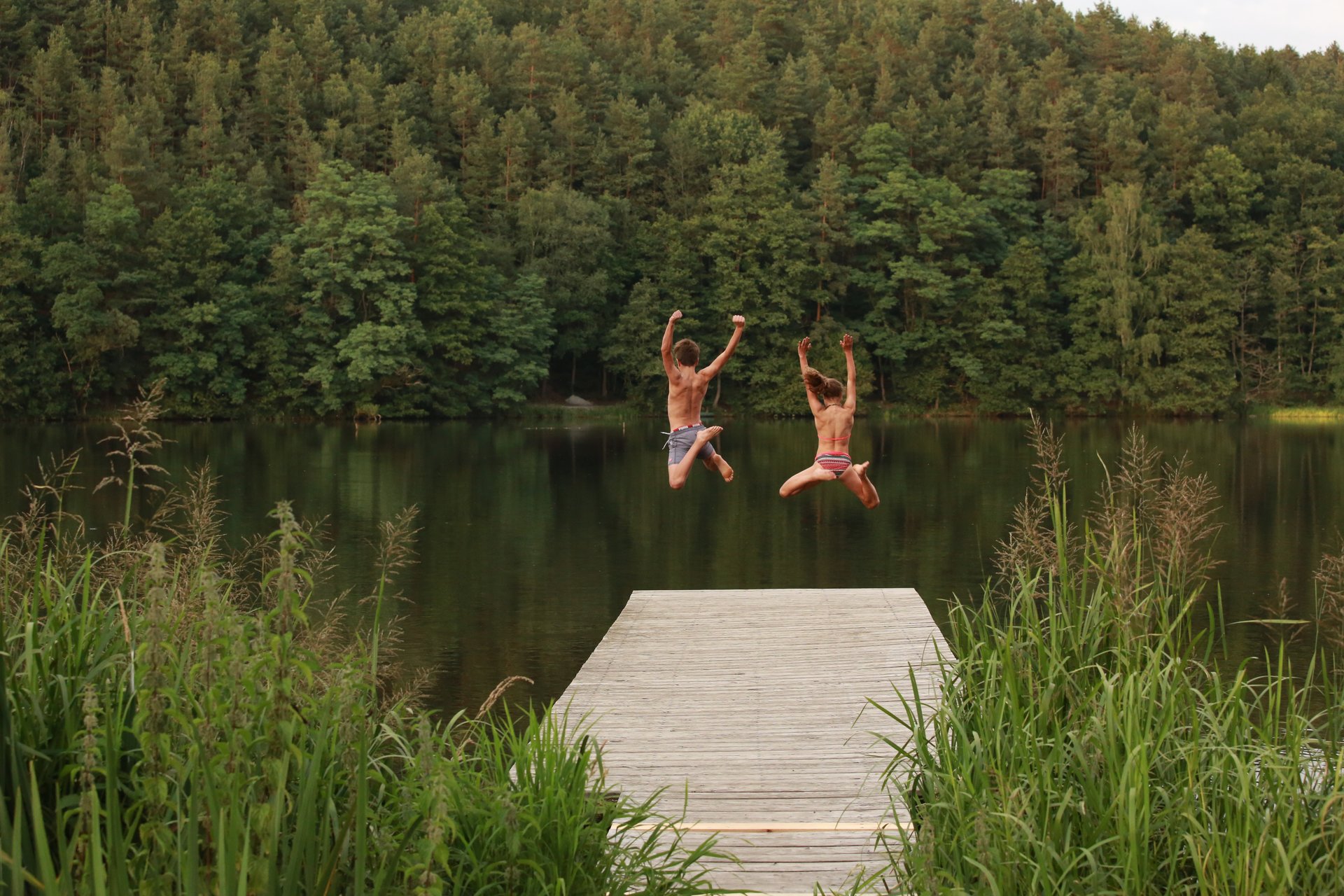 zwei Kinder springen vom Steg aus in den See