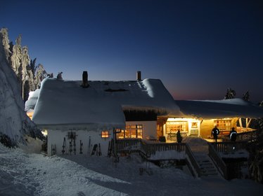 Blick auf das verschneite Gebäude bei Nacht, die Räume innen sind erleuchtet