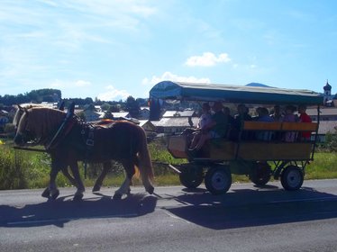 Überdachte Kutsche, voll besetzt mit Menschen, gezogen von zwei starken Pferden