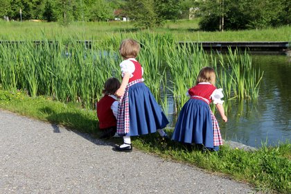 Kinder in Tracht spielen im Schilf an einem See im Kurpark Grafenwiesen
