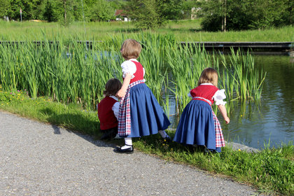 Kinder in Tracht spielen im Schilf an einem See im Kurpark Grafenwiesen
