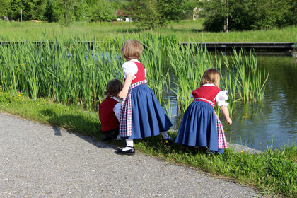 Kinder in Tracht spielen im Schilf an einem See im Kurpark Grafenwiesen