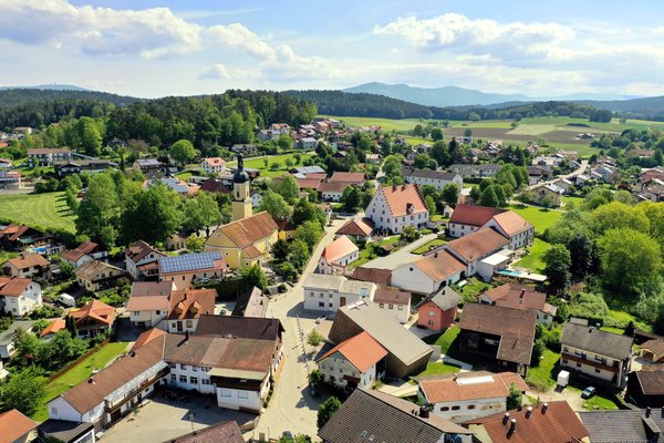 Luftaufnahme in das Zentrum von Blaibach. Blick auf die Häuserdächer und im Hintergrund auf die Bergkette.