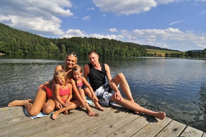 Familie sitzt auf dem Steg, im Hintergrund ist der See