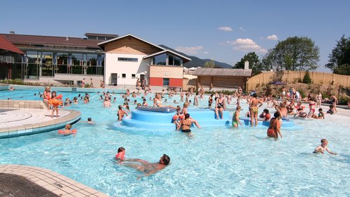 Blick auf das Außenbecken vom Freibad mit vielen Badegästen