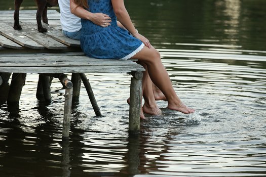 Paar sitzt auf dem Steg und hält die Füße ins Wasser