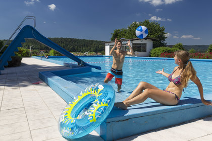 Ein Paar spielt im Wasser Ball, am Beckenrand liegt ein Schwimmreifen