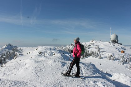Frau mit Schneeschuhen steht am Gipfel vom Arber und schaut in die verschneite Winterlandschaft