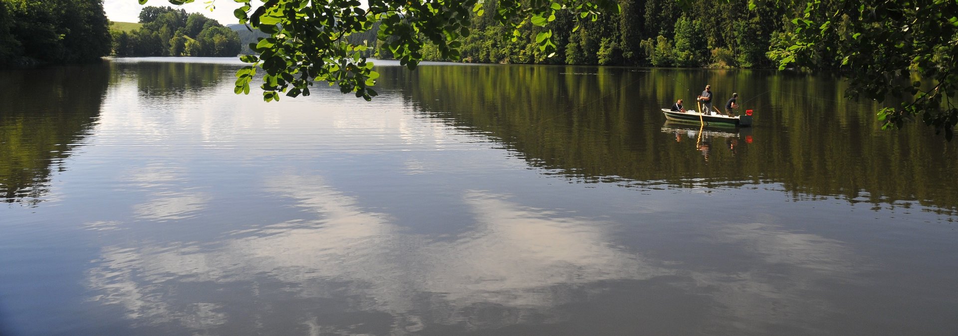 Angeln Boot mit Angler auf einem See mit Bäumen im Hintergrund