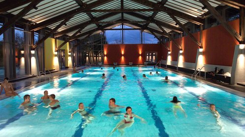 Blick auf das Schwimmerbecken im AQACUR mit einigen Badegästen, es dämmert bereits und die Halle ist schön beleuchtet