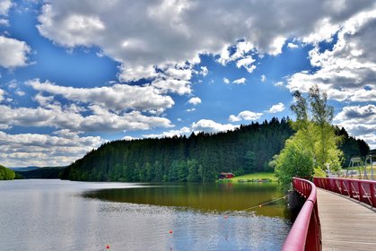 Blick über die rote Brücke hin zum See am Badeufer sieht man die rote Scheune, in der die Boote gelagert werden