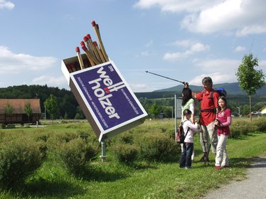 Blick auf die Außenwerbung in Form einer Zündholzschachtel, davor steht eine Familie