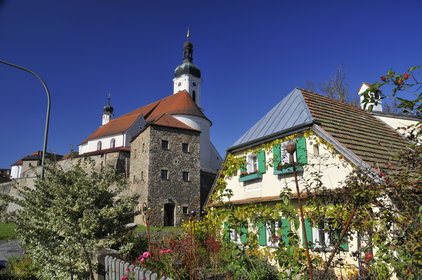 Blick auf die Kirche und die Burgmauern, im Vordergrund sieht man ein kleines Haus