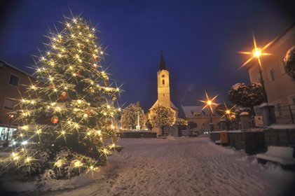 Blick auf den verschneiten Marktplatz im dunkeln, der Christbaum ist beleutet und die Kirche ist im Hintergrund zu sehen