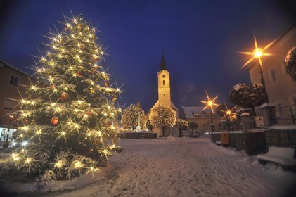 Blick auf den verschneiten Marktplatz im dunkeln, der Christbaum ist beleutet und die Kirche ist im Hintergrund zu sehen